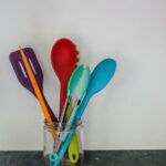 Colorful kitchen utensils in a glass jar against a neutral background.